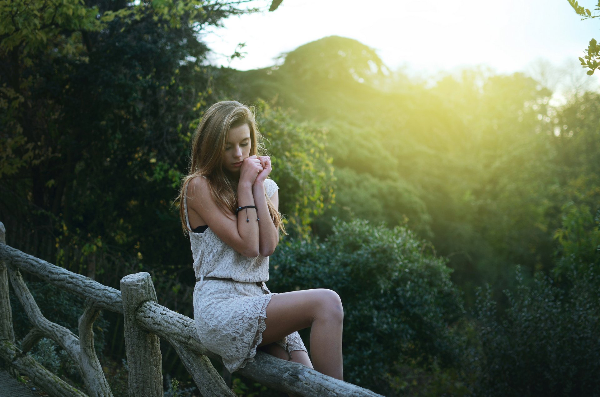 girl blonde beautiful pretty slender figure pose sitting legs hands dress face look forest park jungle summer sun light tree fence fence light slender figure represent hips view l