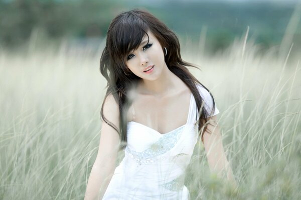 A girl of Asian appearance is standing in a meadow in the grass