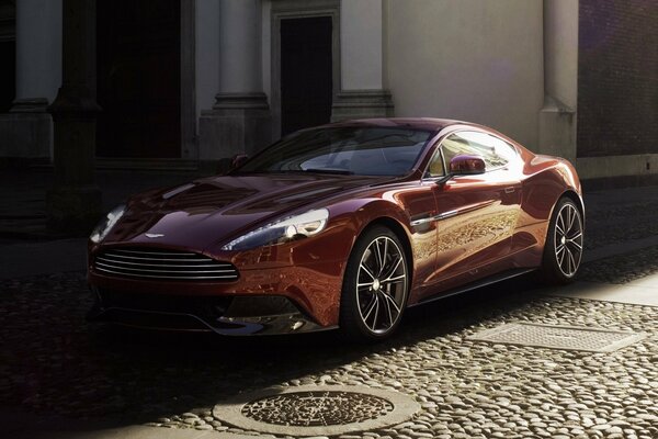 Burgundy Aston Martin Vanquish on a cobblestone road in the shade