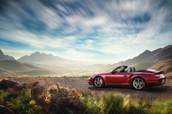 La Porsche convertibile rossa guida su una strada sabbiosa