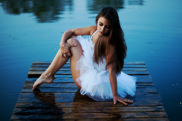Девушка балерина сидит у озера на пирсе