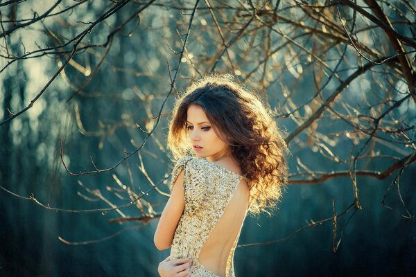 Fille dans une robe avec un grand décolleté dans le dos sur un fond flou de branches sans feuilles