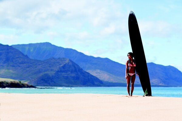 Chica con una tabla de surf en el fondo de las montañas y el océano