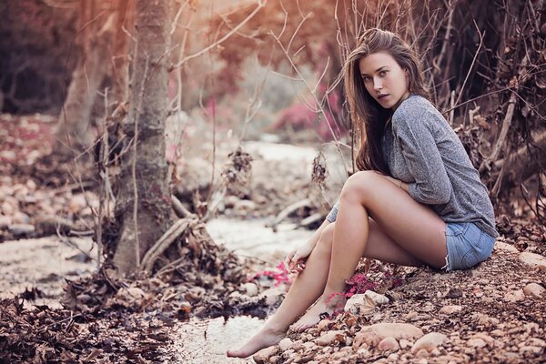 A girl in shorts is sitting on rocks in the forest