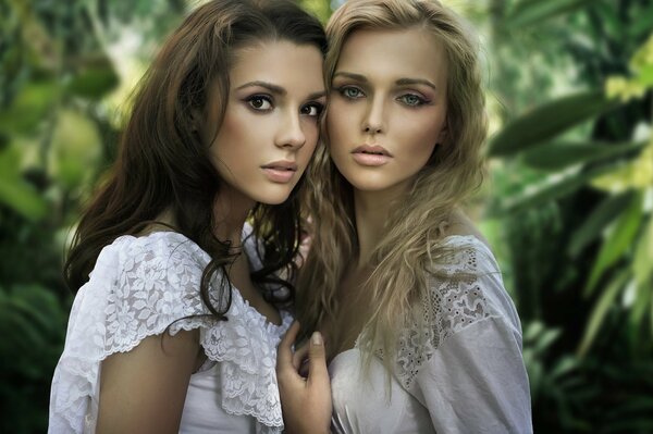 Blonde and brunette with a gentle look on a background of greenery