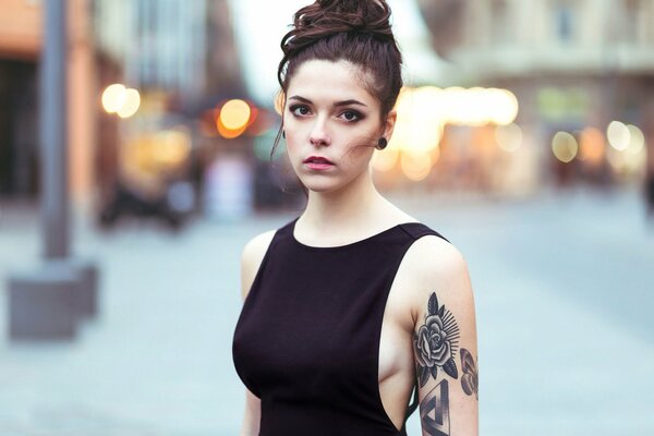 A girl with a bun in a black T-shirt and a tattoo of a rose