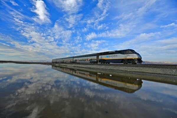 Le train longe le lac dans lequel les nuages se reflètent