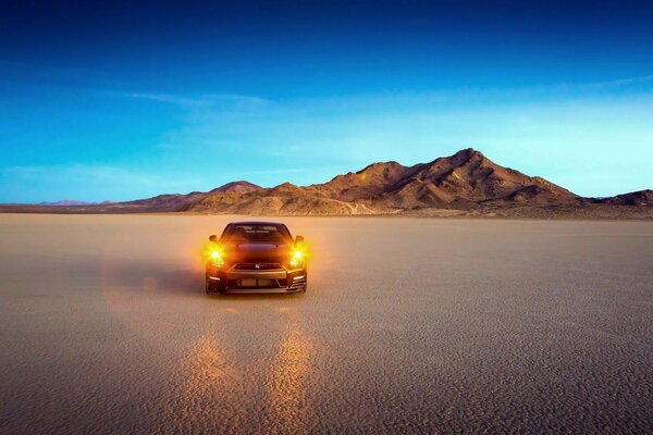 A car with its headlights on in the desert
