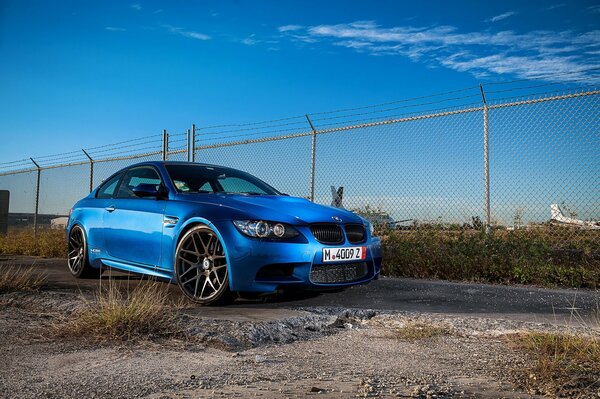 Blue car at the fence against the sky