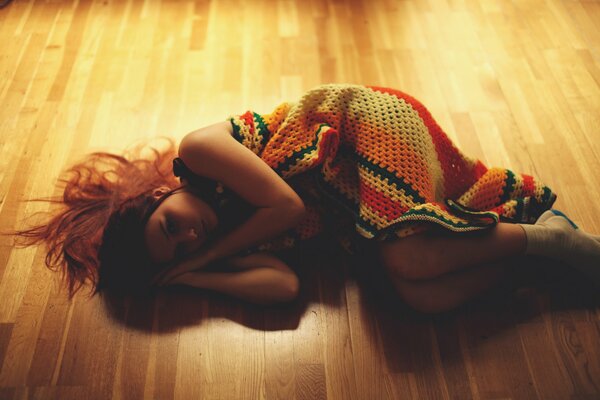 The girl wrapped in a knitted rug lies curled up on the floor