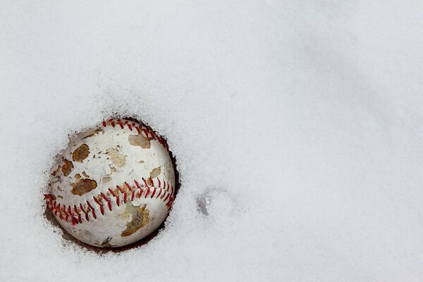Потрескавшийся старый бейсбольный мяч в снегу