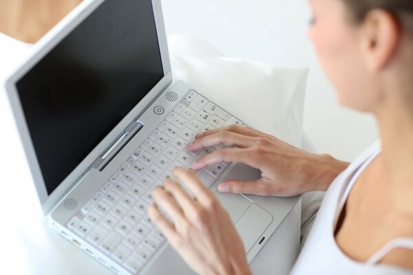 Una ragazza con le mani magre scrive su un computer portatile bianco