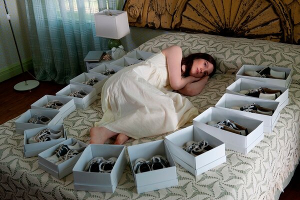 A beautiful girl is lying on a bed with a lot of boxes with shoes