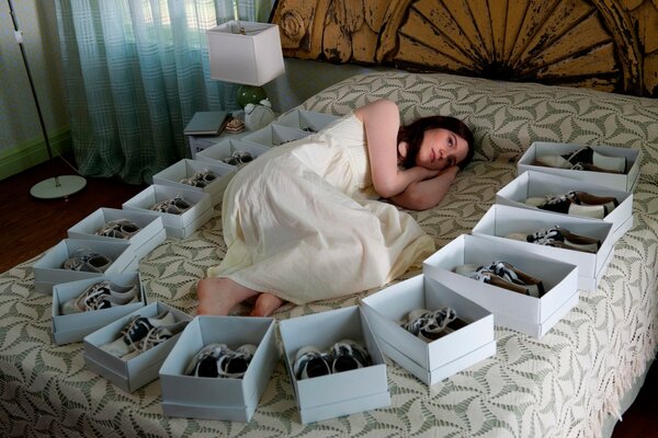 Hermosa chica se acuesta en la cama con cajas de zapatos
