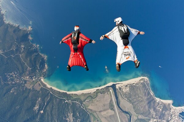 Wingsuits hover over the beach and the sea