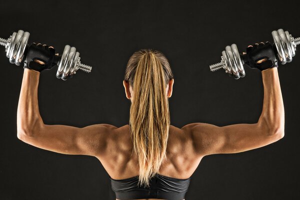 Athletic and muscular blonde holds dumbbells from the back