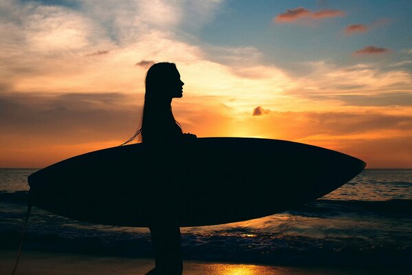 Silhouette de jeune fille avec planche de surf sur fond de mer et coucher de soleil luxueux