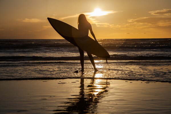 A girl stands on the sand by the sea with a board