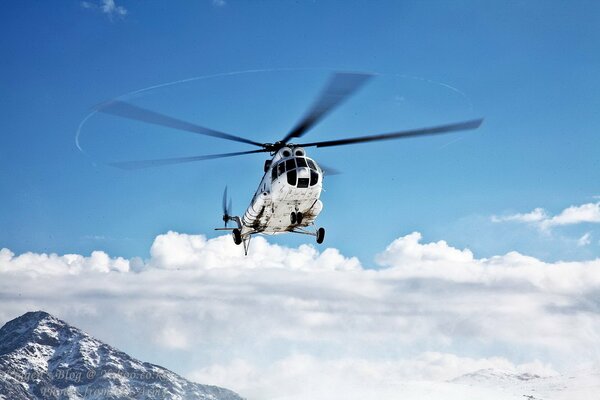 The helicopter flies in the air over clouds and mountains