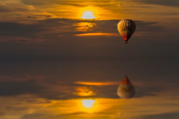 Reflexion im Wasser eines bei Sonnenuntergang fliegenden Ballons