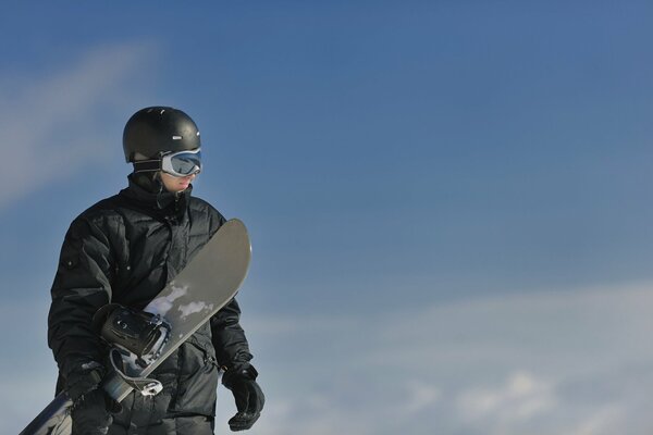 Snowboardzista stoi ze snowboardem na tle nieba