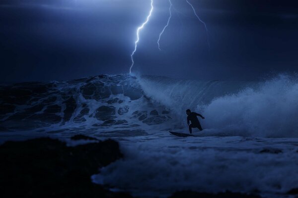 Der Typ surft und erobert nachts im Meer bei einem Gewitter eine Welle