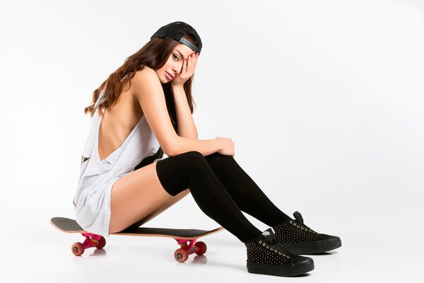 Una ragazza in calze nere si siede su uno skateboard