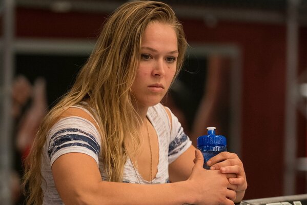 Brüstendes Foto der amerikanischen Wrestlerin Ronda Rosie im weißen T-Shirt mit einer blauen Wasserflasche in den Händen