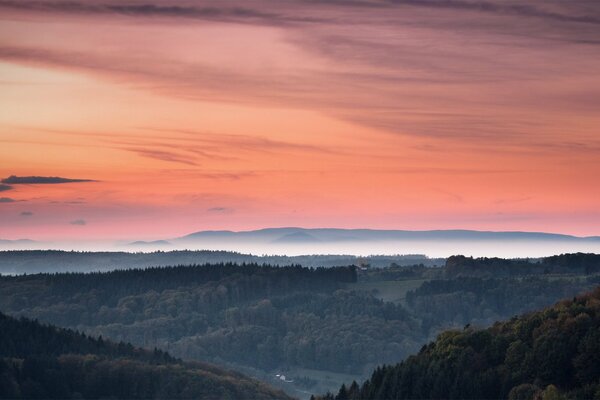 Der orange Sonnenuntergang ist am Himmel eingefroren. Dunst umhüllt die Hügel und den geheimnisvollen Wald