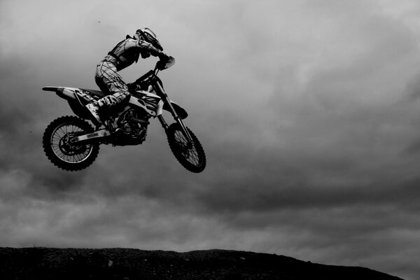 Fotografía artística en blanco y negro de un hombre en un casco de motocicleta en una motocicleta en el punto superior de un salto de truco