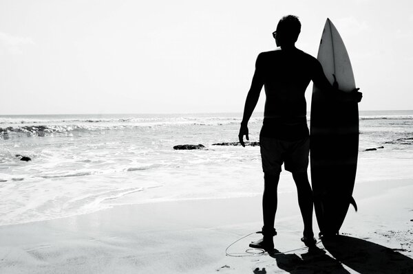 Black and white photo of a surfer with a board on the beach