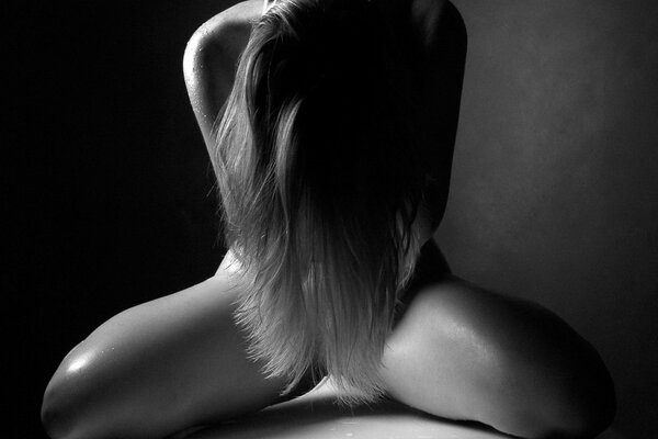 Ein nacktes Mädchen bedeckt mit langen Haaren ihre intimen Orte auf einem Schwarz-Weiß-Foto