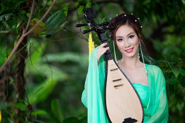 Chica asiática en verde toca un instrumento musical