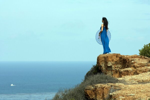 The girl stands on the birch of the sea and looks into the distance