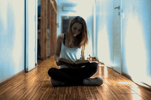 Jeune fille est assise dans le couloir sur le sol et lit un livre