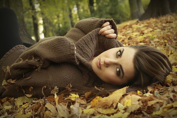 A girl in a sweater poses in leaves