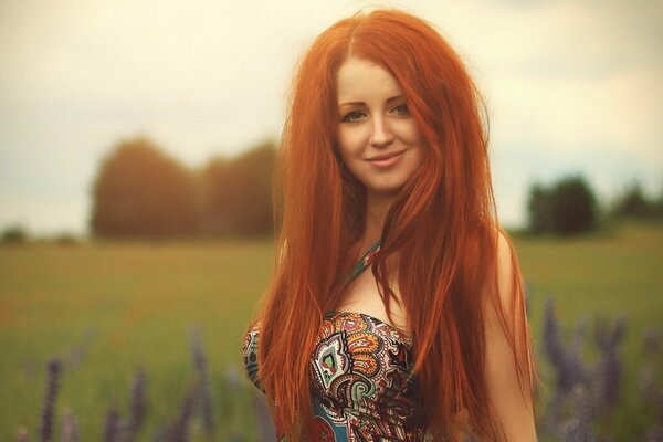 Hermosa chica con el pelo largo rojo, con una sonrisa elegante, en el fondo del campo