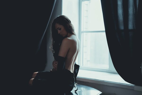 A young darling is sitting at the window with her back naked