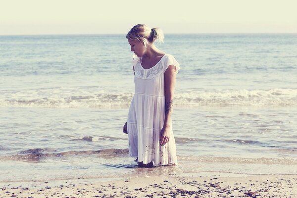 A girl in a white dress poses against the background of sea waves