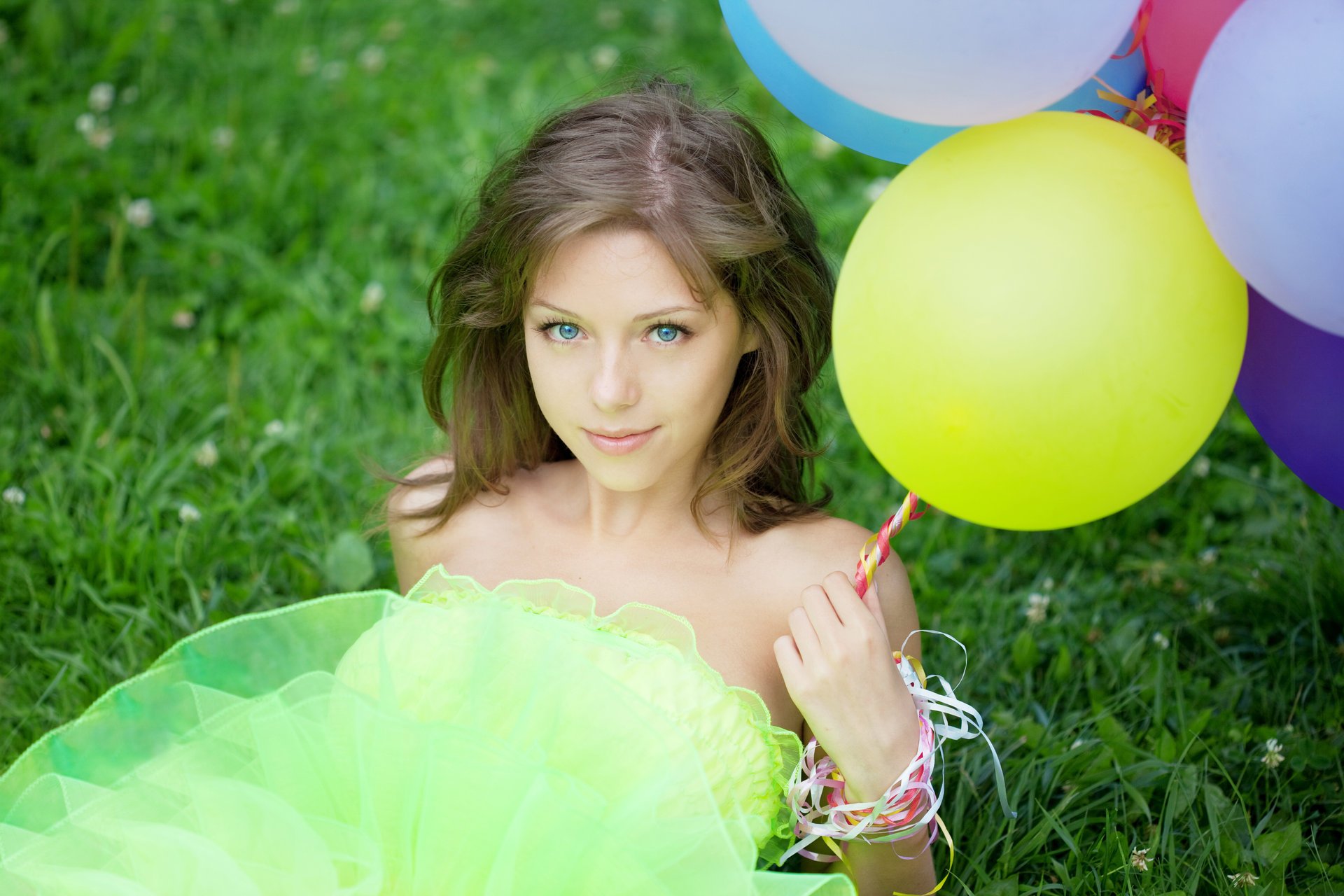 chica ojos azules pelo castaño globos hierba trébol mirada. sonrisa rizos