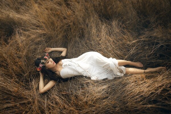 A girl in a white dress is lying on the grass