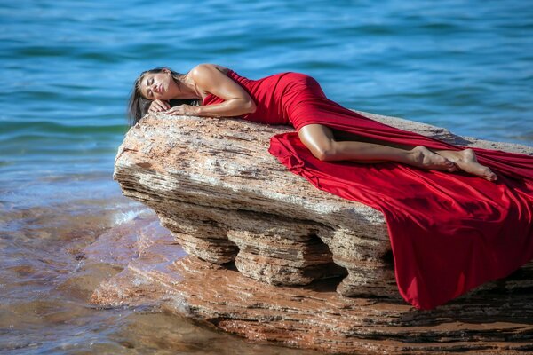 Fille en robe rouge sur un rocher sur fond de mer