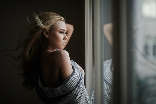 Fille aux cheveux blonds regarde par la fenêtre