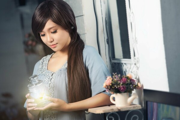 Belle asiatique se tient près d un vase de fleurs et tient doucement une carafe