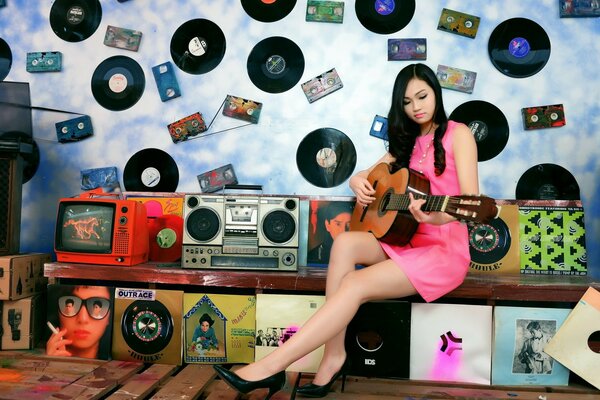 The girl plays the guitar against the background of retro receivers, records and cassettes