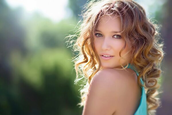 A girl in a turquoise dress and with curls poses