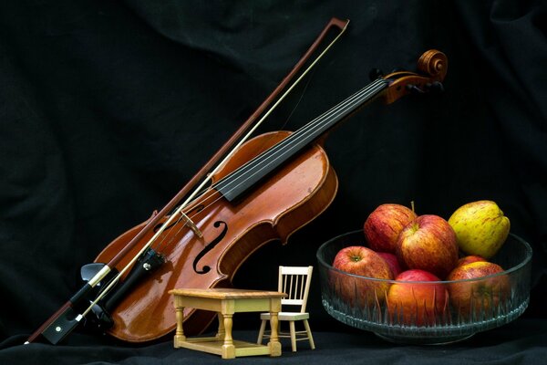 Violín, manzanas, mesa con silla sobre fondo negro