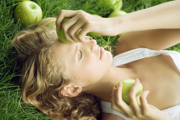 The girl is lying on the grass with apples in her hands