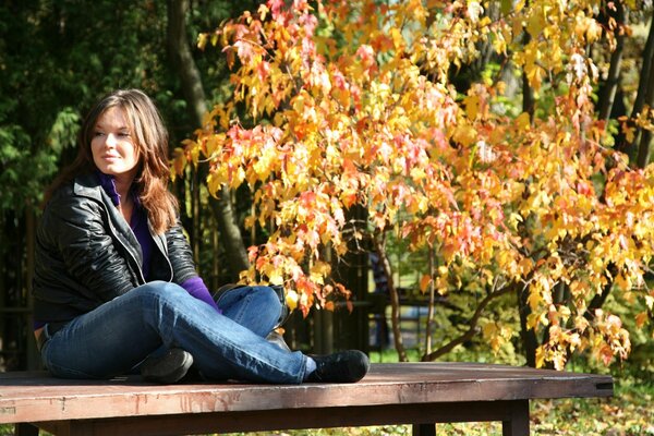 Chica sentada en un banco en el otoño