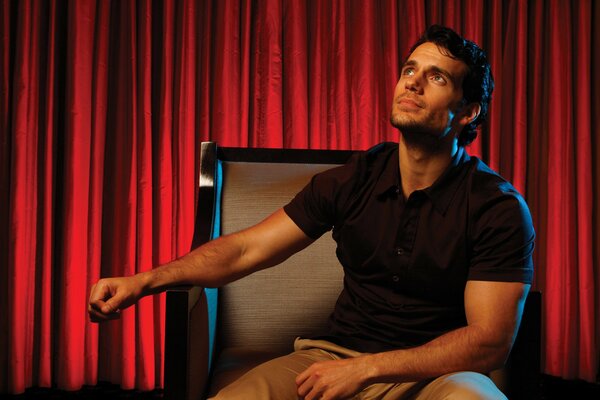 Henry Cavill en una silla con cortinas rojas